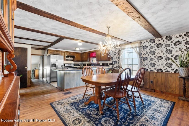 dining area with an inviting chandelier, beamed ceiling, light wood finished floors, wainscoting, and wood walls