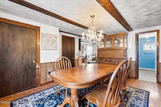 dining area featuring beam ceiling, wainscoting, a chandelier, and wood finished floors