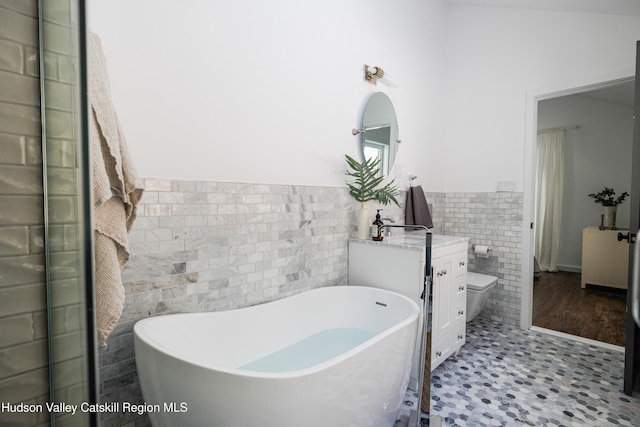 bathroom with a tub, toilet, vanity, and tile walls