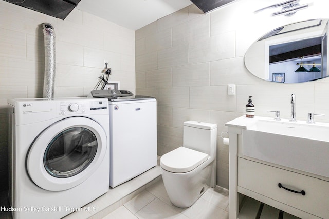 clothes washing area featuring separate washer and dryer, tile walls, and light tile patterned floors