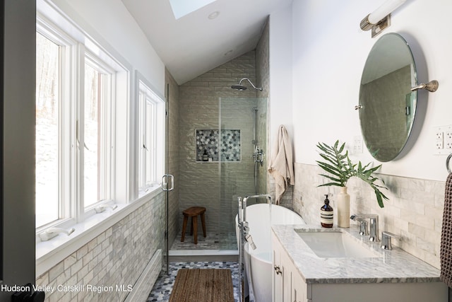 bathroom with tile patterned flooring, tile walls, vaulted ceiling with skylight, shower with separate bathtub, and vanity