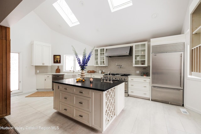 kitchen with white cabinets, a kitchen island, wall chimney range hood, a skylight, and high quality appliances