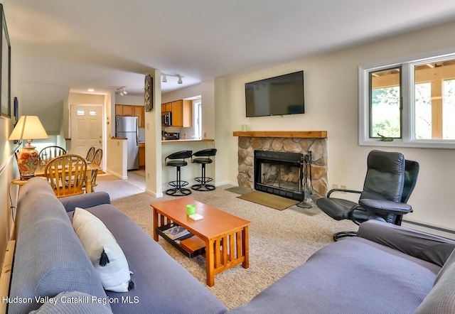 living room with light carpet, a stone fireplace, and baseboard heating