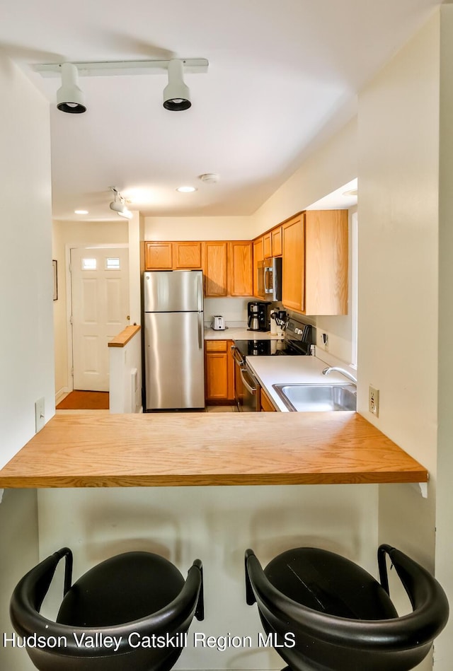 kitchen with stainless steel appliances, a sink, a peninsula, a breakfast bar area, and recessed lighting