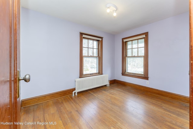 empty room featuring radiator, wood finished floors, plenty of natural light, and baseboards