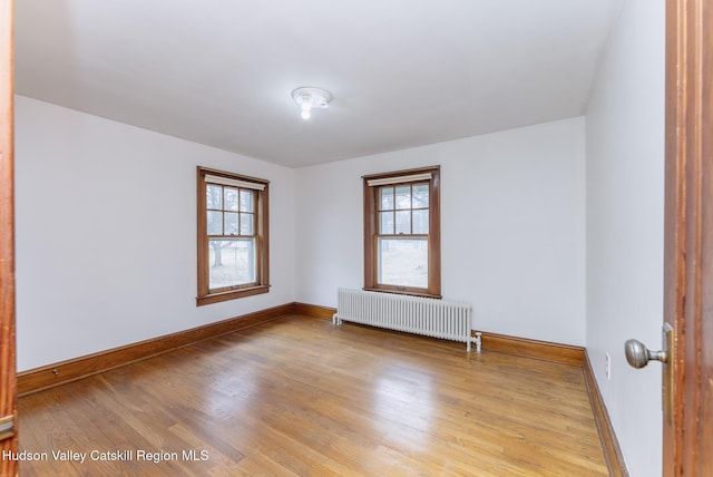 empty room with a wealth of natural light, radiator heating unit, baseboards, and wood finished floors