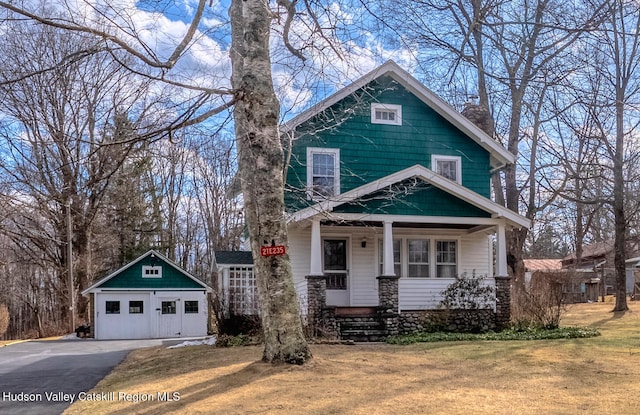 view of front of property featuring an outbuilding, a porch, a detached garage, and a front yard