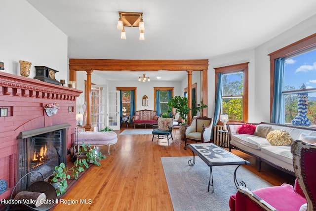 living room with light wood finished floors, a brick fireplace, and decorative columns