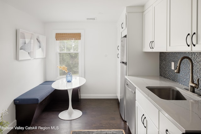 kitchen featuring white cabinetry, sink, light stone countertops, stainless steel dishwasher, and decorative backsplash