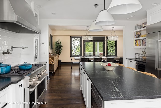 kitchen with high end appliances, wall chimney exhaust hood, tasteful backsplash, a kitchen island, and white cabinetry