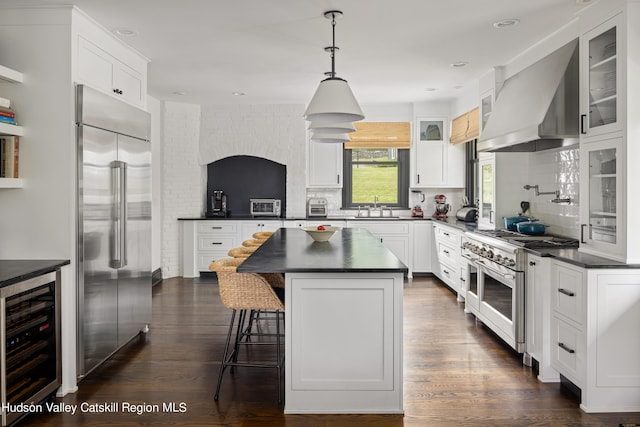 kitchen featuring wall chimney exhaust hood, premium appliances, a kitchen island, white cabinetry, and beverage cooler