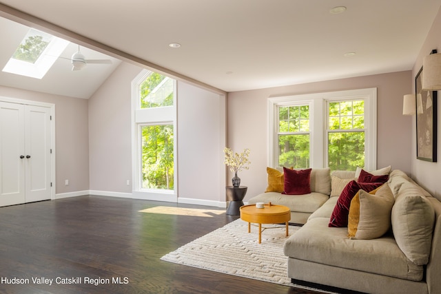 living room with ceiling fan, vaulted ceiling with skylight, and dark wood-type flooring