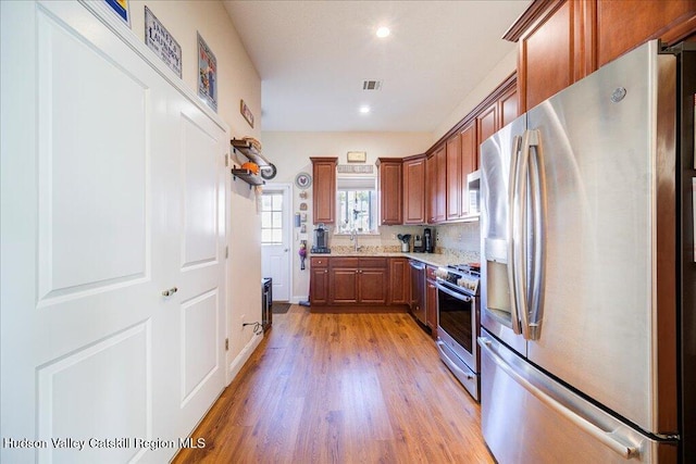 kitchen with stainless steel appliances, light hardwood / wood-style floors, light stone counters, and sink