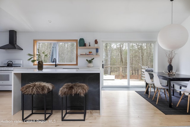 kitchen with wall chimney exhaust hood, white gas range oven, a wealth of natural light, and light hardwood / wood-style flooring