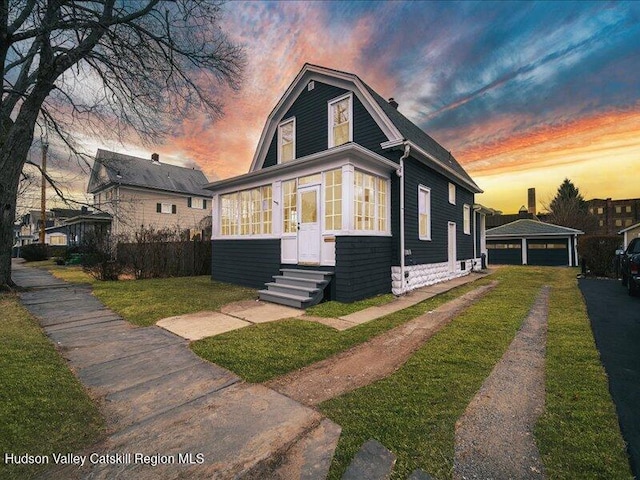 bungalow-style house featuring a lawn, a garage, and an outbuilding