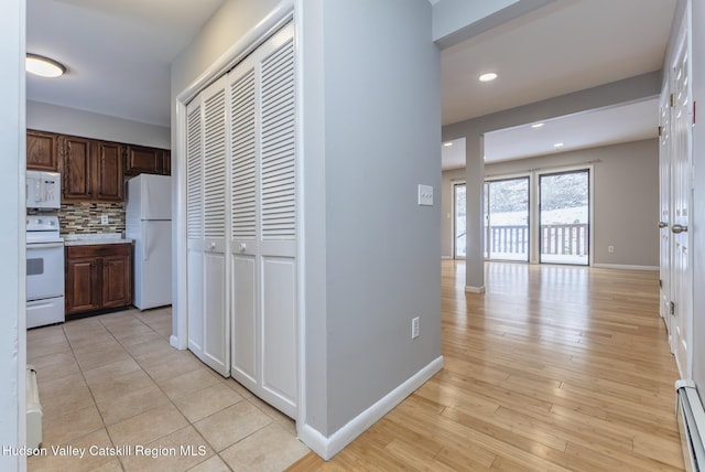 kitchen featuring white appliances, baseboard heating, dark brown cabinetry, decorative backsplash, and light wood-type flooring