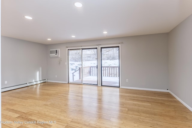 empty room with baseboard heating, light hardwood / wood-style floors, and an AC wall unit