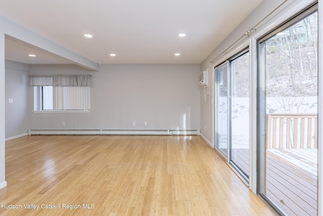 empty room with light wood-type flooring, a wall unit AC, and a baseboard heating unit