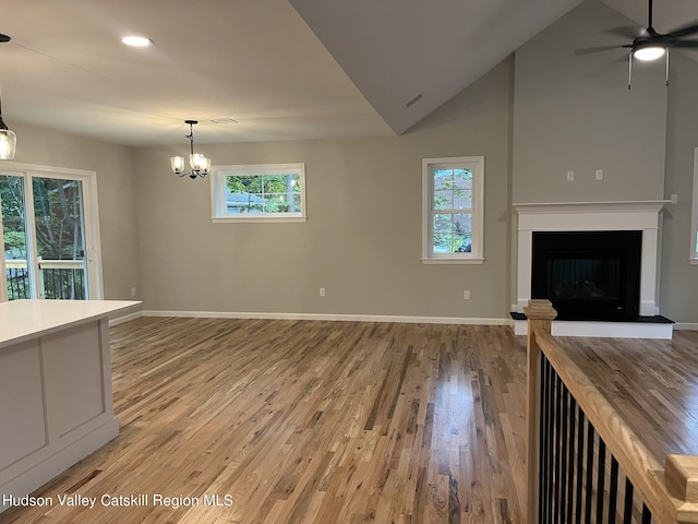 unfurnished living room featuring hardwood / wood-style flooring, ceiling fan with notable chandelier, and high vaulted ceiling