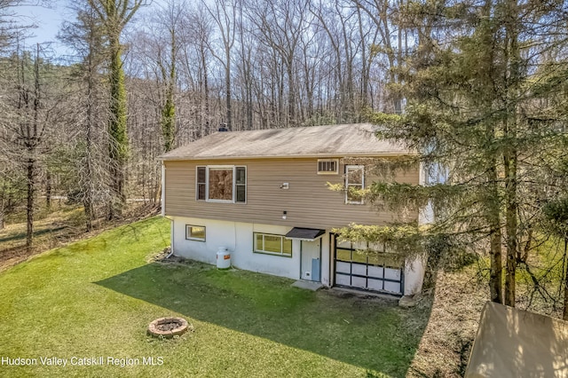 back of property with a wooded view, a yard, driveway, and a garage