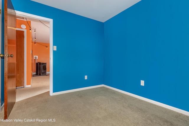 carpeted empty room featuring a wood stove and baseboards