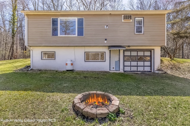 rear view of property with a lawn, stucco siding, a fire pit, and a garage