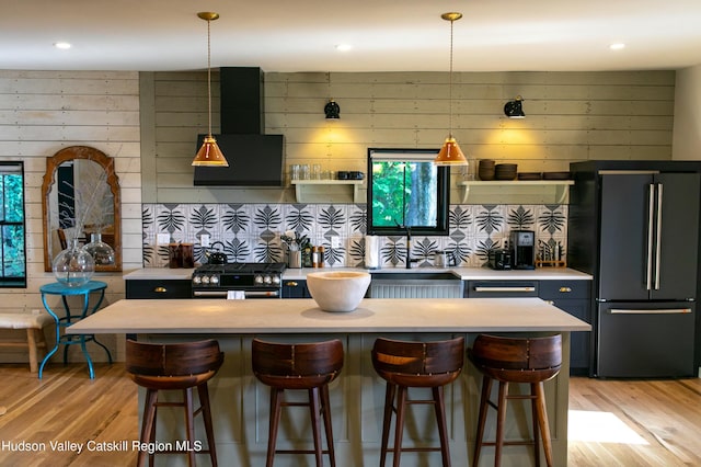 kitchen with sink, wall chimney exhaust hood, pendant lighting, a breakfast bar area, and black appliances