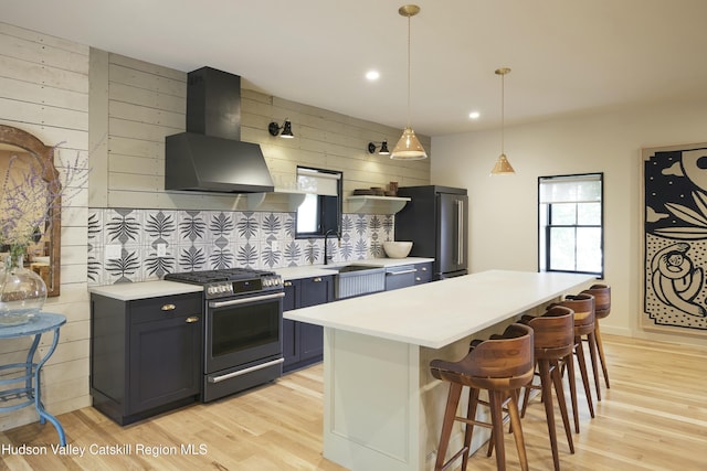 kitchen with a kitchen island, stainless steel appliances, wall chimney range hood, and a breakfast bar area