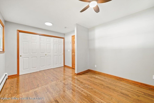 unfurnished bedroom with hardwood / wood-style flooring, ceiling fan, baseboard heating, and a closet