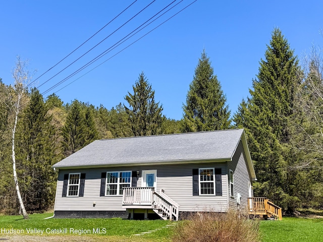 view of front facade with a wooded view, a front yard, and a deck