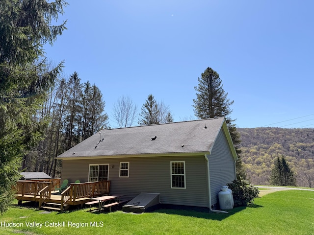 back of house featuring a lawn, a wooden deck, and a wooded view