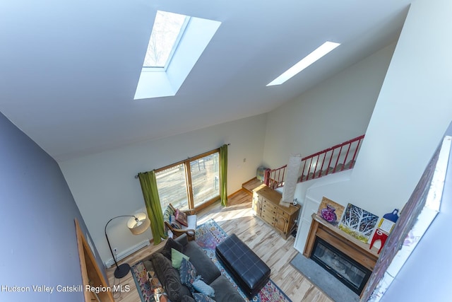 living room featuring a fireplace, light hardwood / wood-style floors, high vaulted ceiling, and a skylight