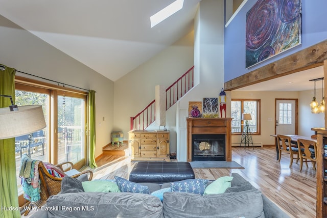 living room with baseboard heating, a skylight, high vaulted ceiling, and light wood-type flooring