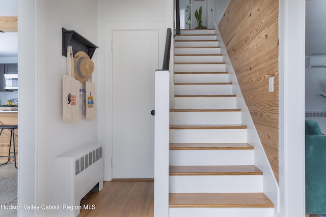 stairs with wooden walls, radiator heating unit, and hardwood / wood-style floors