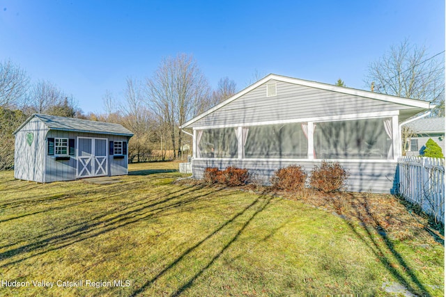 view of side of property featuring fence, a lawn, an outbuilding, and a sunroom