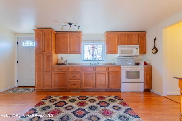 kitchen with light wood-style flooring, a sink, white appliances, light countertops, and baseboards