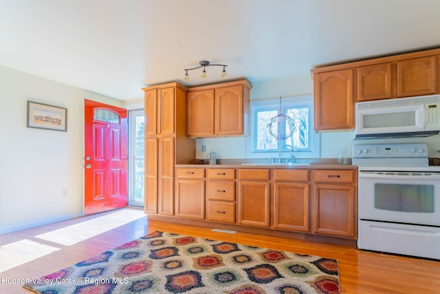 kitchen featuring visible vents, a sink, white appliances, light wood-style floors, and baseboards