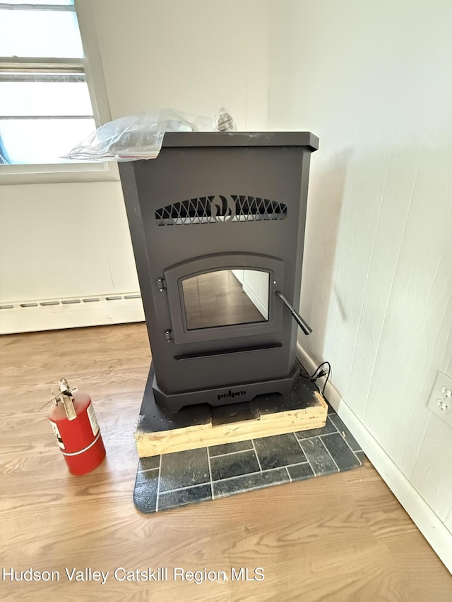 details with a wood stove, hardwood / wood-style floors, and a baseboard heating unit