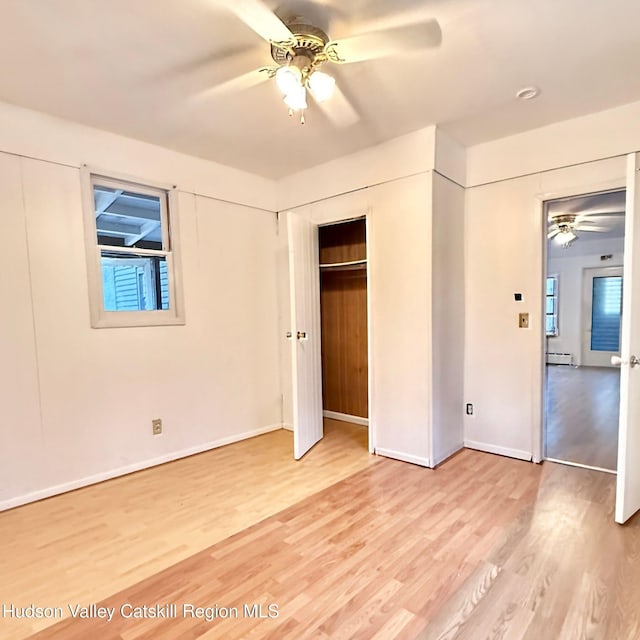 unfurnished bedroom with a closet, a baseboard heating unit, baseboards, multiple windows, and light wood-type flooring