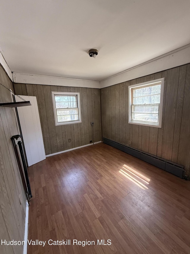 unfurnished bedroom with wooden walls, wood finished floors, and a baseboard heating unit