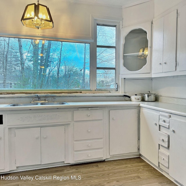 kitchen with sink, light hardwood / wood-style flooring, a notable chandelier, white cabinetry, and hanging light fixtures