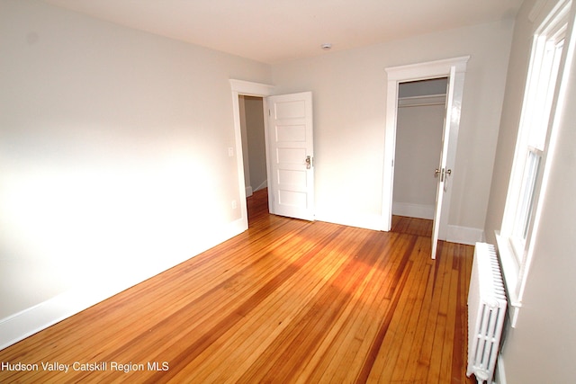 unfurnished bedroom with a closet, radiator, and light hardwood / wood-style floors