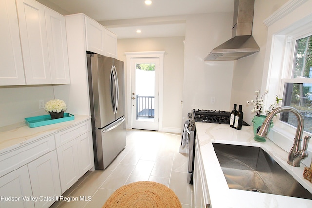 kitchen with sink, wall chimney range hood, light stone counters, white cabinets, and appliances with stainless steel finishes