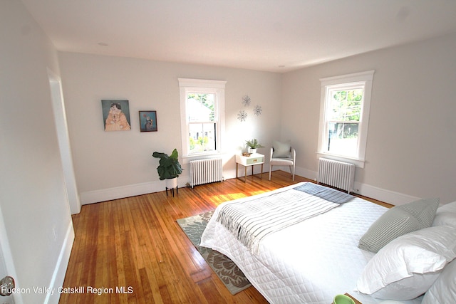 bedroom with multiple windows, hardwood / wood-style floors, and radiator