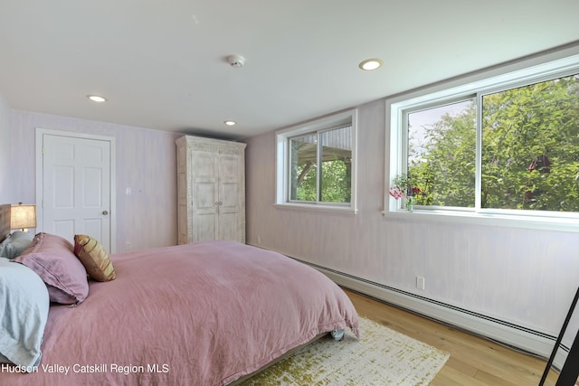 bedroom featuring light hardwood / wood-style floors, baseboard heating, and multiple windows