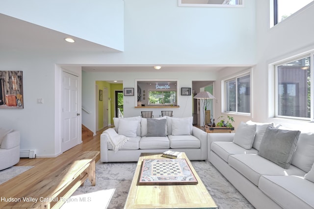 living room with baseboard heating, light hardwood / wood-style floors, and a high ceiling