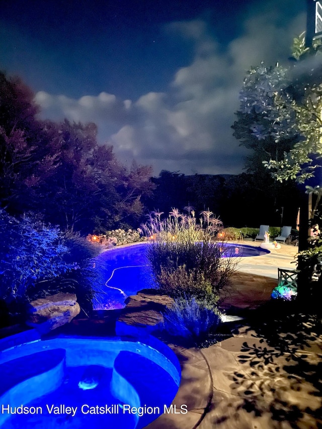 pool at twilight featuring a hot tub