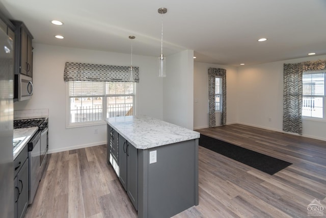 kitchen featuring stainless steel microwave, a center island, wood finished floors, open floor plan, and gray cabinets