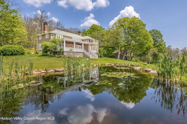 rear view of property featuring a water view, a yard, and a chimney