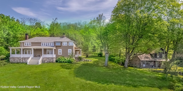 view of front of property with a front yard, a view of trees, a chimney, and covered porch